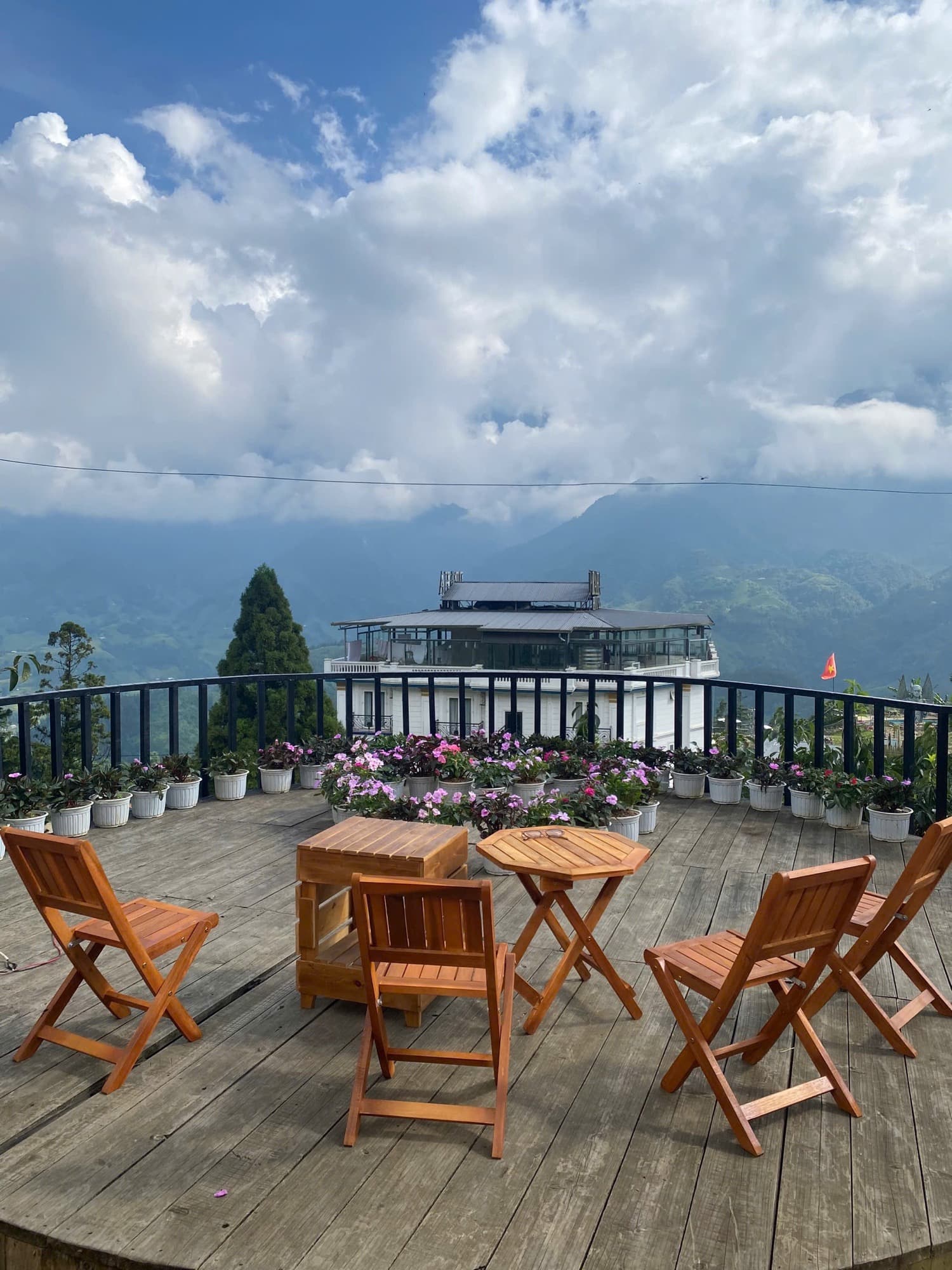 Sân gỗ chung với bàn ghế, dãy chậu hoa và lan can nhìn ra núi.